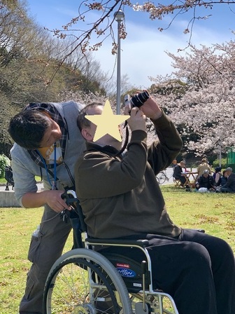 車椅子の男性がカメラで桜の枝を撮影している