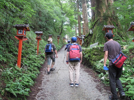 両脇に木製の赤い灯籠が並んだ坂道を上る、4人の後ろ姿。