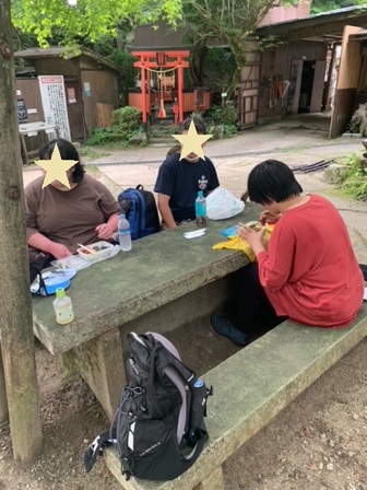 赤い鳥居の祠の正面にある、コンクリート製のテーブル・ベンチで昼食をとっている参加者3人。